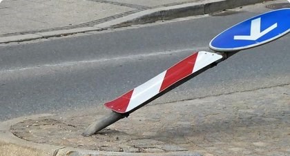 Umgeknicktes Verkehrsschild mit rot-weißer Leitbake auf einer Verkehrsinsel